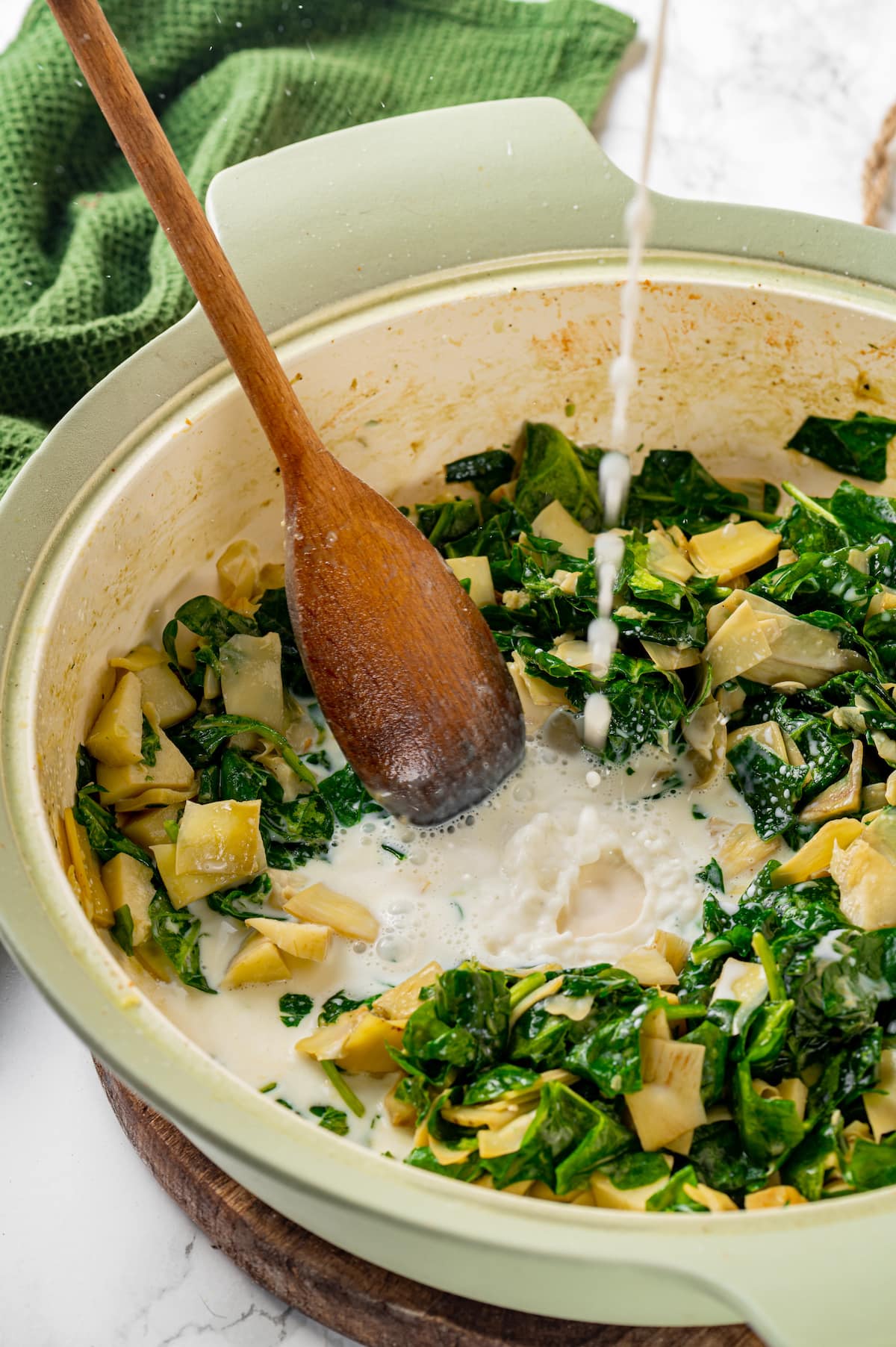 Milk poured into a skillet with spinach artichoke cream sauce.