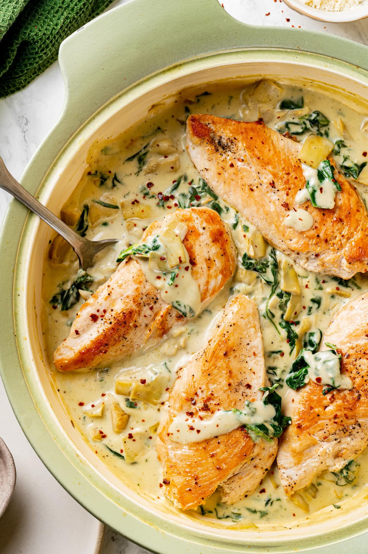 Overhead view of creamy spinach artichoke chicken in a large skillet.