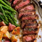 Marinated grilled steak on a serving plate with a side of asparagus and potatoes.