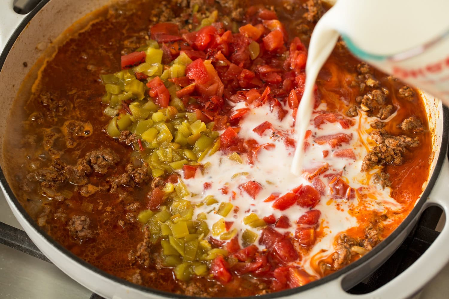 Liquid, tomatoes, and green chilies added to beef in pan.