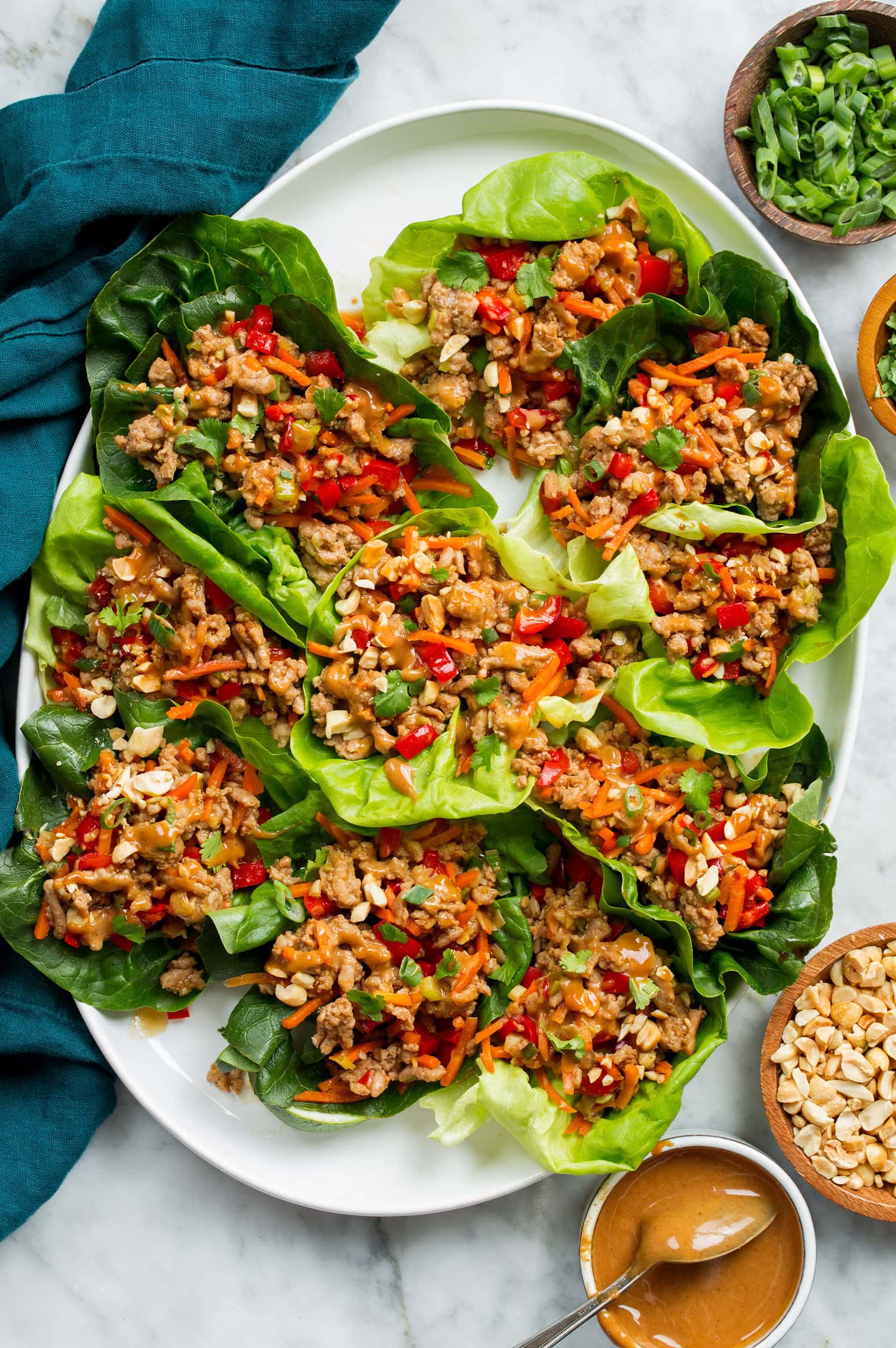 Thai lettuce wraps shown from above on a white platter on a marble surface with a blue cloth to the side.