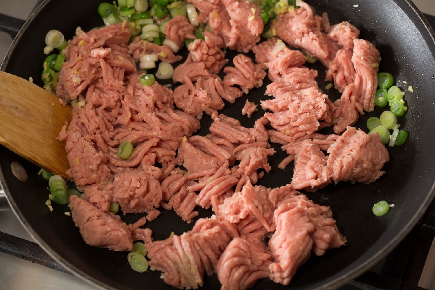 Ground chicken chunks added to a dark skillet.