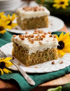 Two slices of homemade zucchini cake with cream cheese frosting with sunflowers decorating plates.