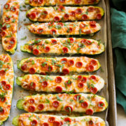 Zucchini Pizza Boats on a large baking sheet with a green cloth to the side.